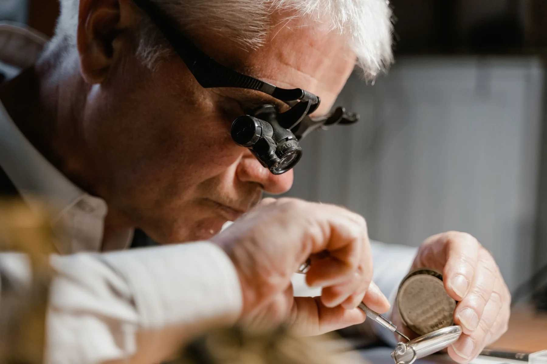 A watchmaker examining a pocket watch through a loupe at the bench