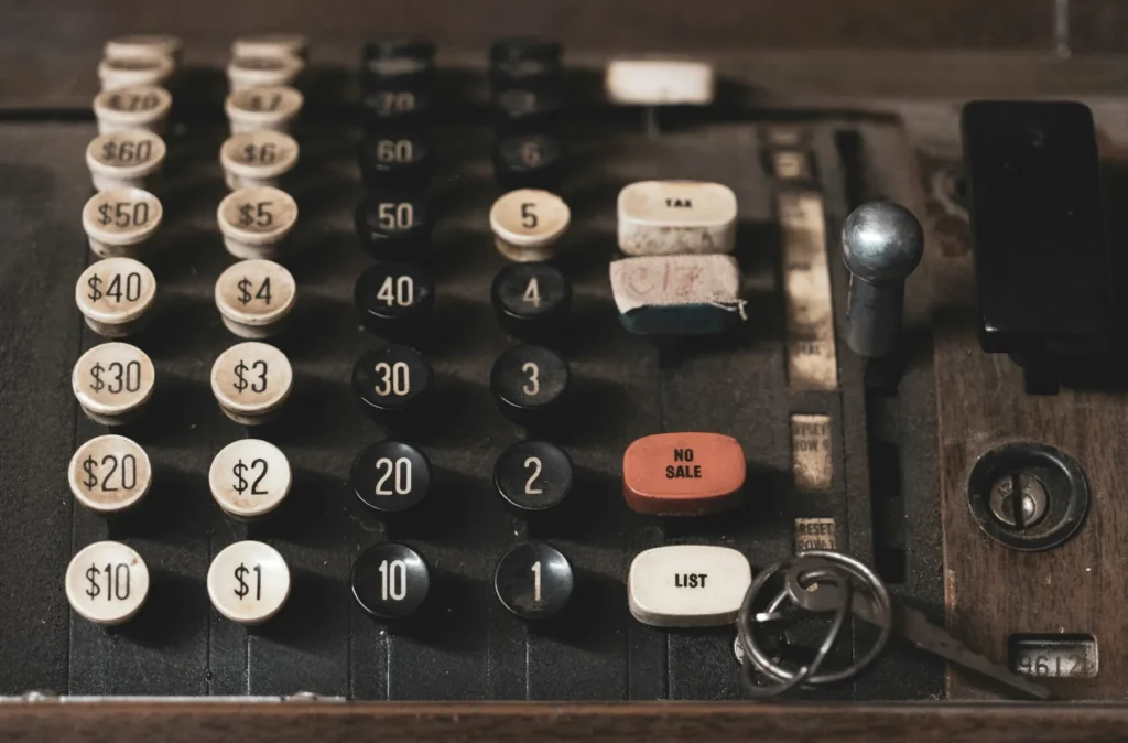The keyboard of an old mechanical cash register: two columns of dollar keys, two of digits, a worn key stamped TAX and a red NO SALE key beside them