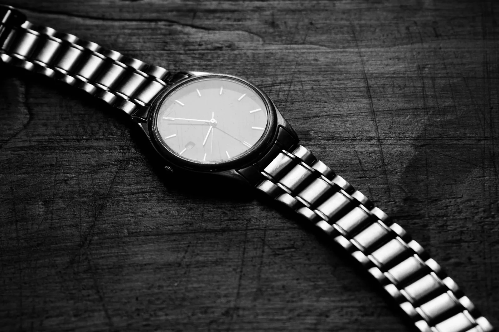 A plain wristwatch on a steel bracelet resting on a dark surface