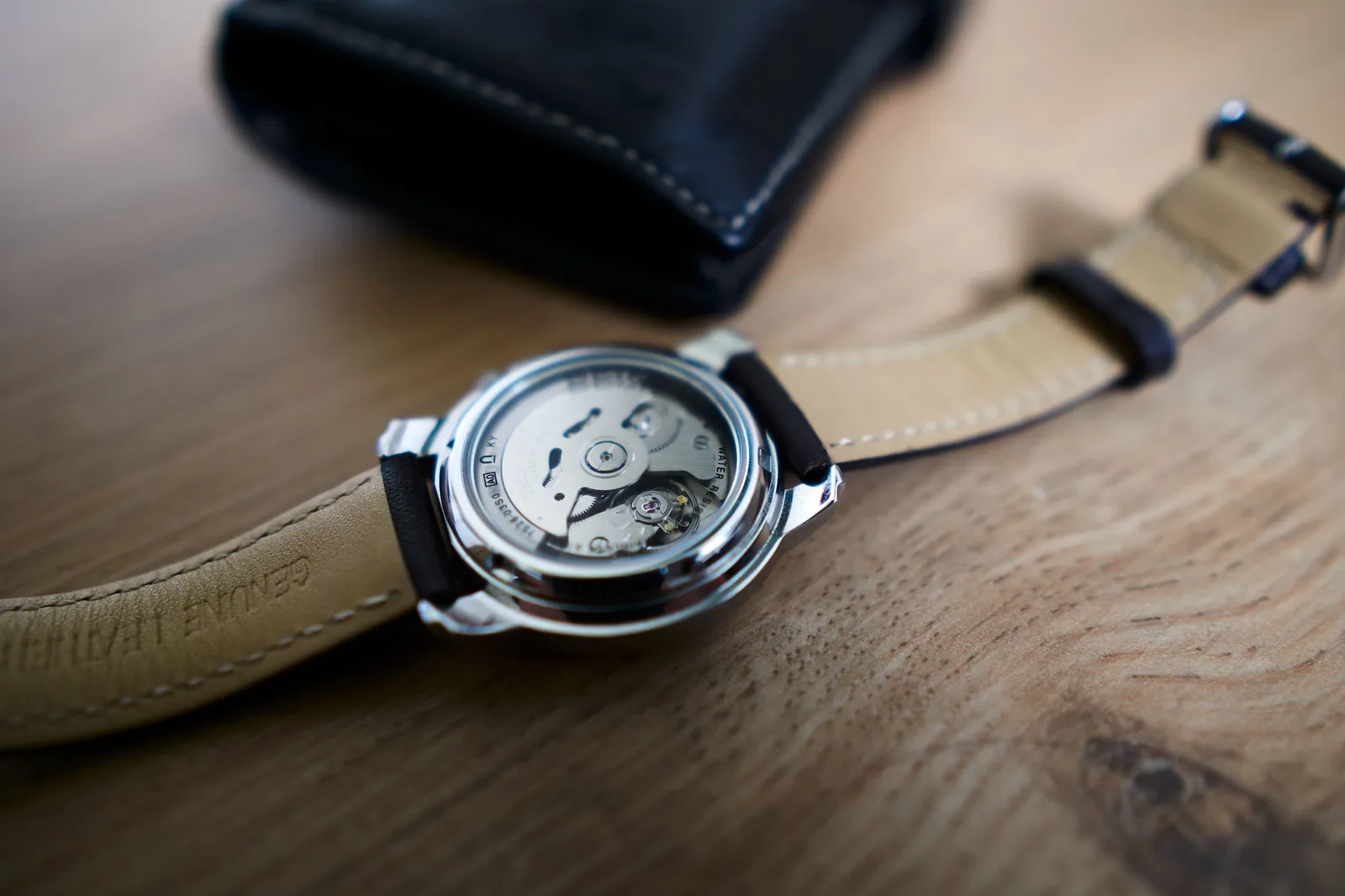 A mechanical wristwatch on a wooden table with its movement visible