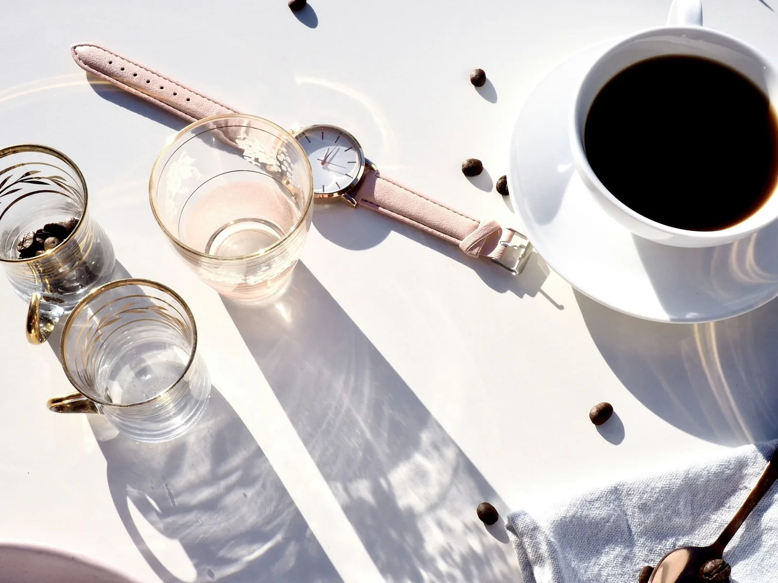 A wristwatch on a table in morning light beside a cup of coffee