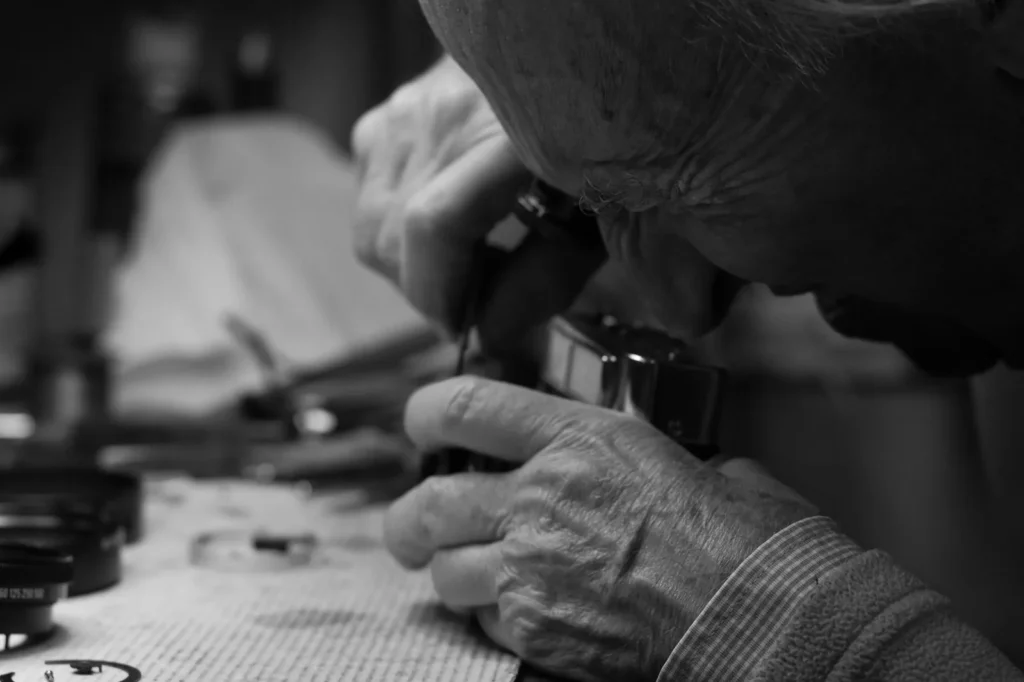 A hand holding a jeweller's loupe over the dial of a wristwatch