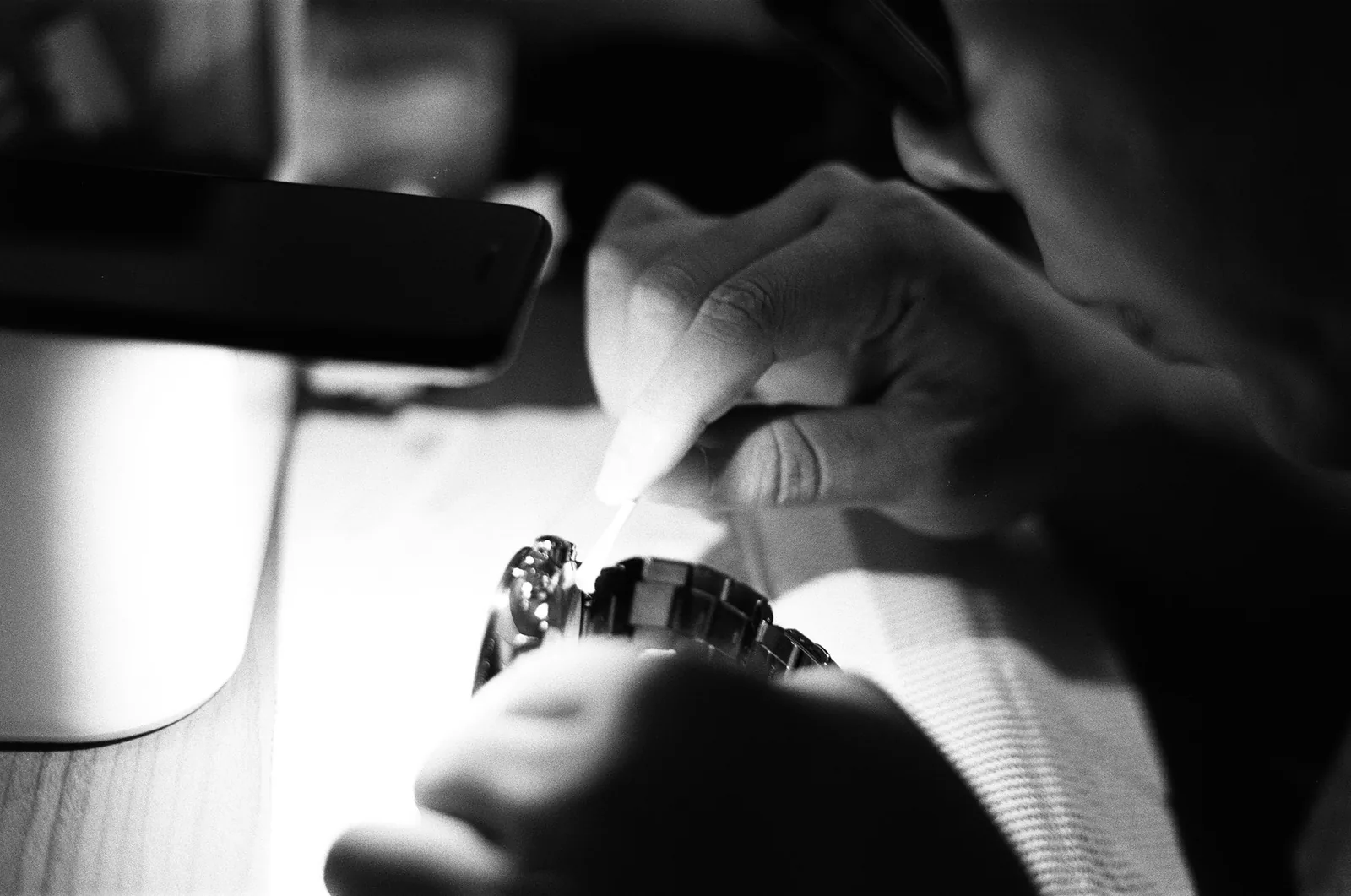 A hand holding a jeweller's loupe over the dial of a wristwatch