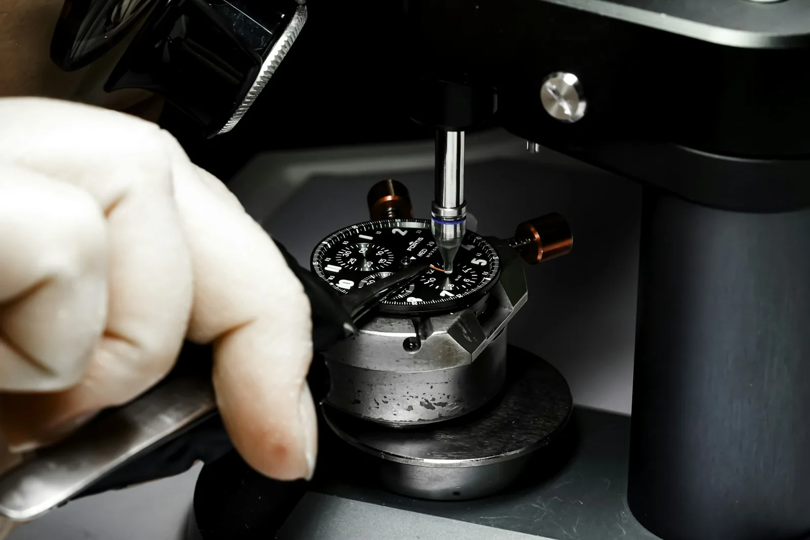 A watchmaker holding tweezers over an open watch movement at a bench