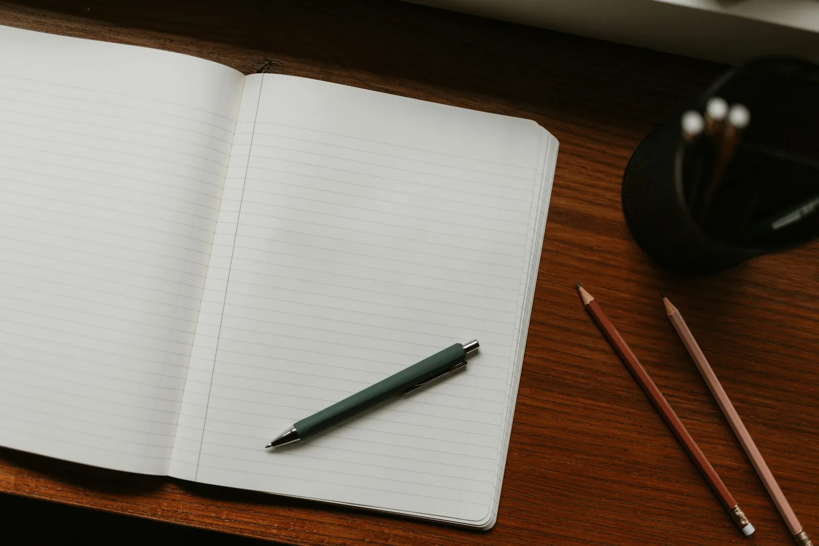 A plain steel wristwatch resting on a worn wooden desk beside a closed notebook