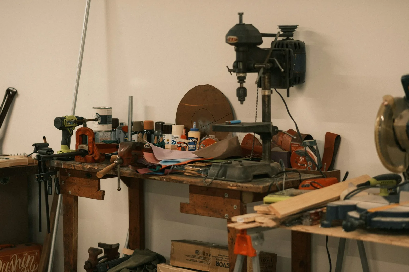 A watchmaker's hands using tweezers over a movement on a cluttered workbench