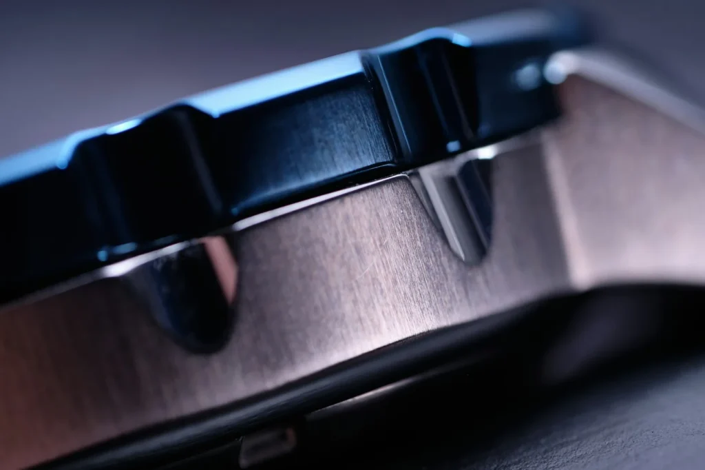 The brushed steel surface of a watch case photographed close up, showing the grain