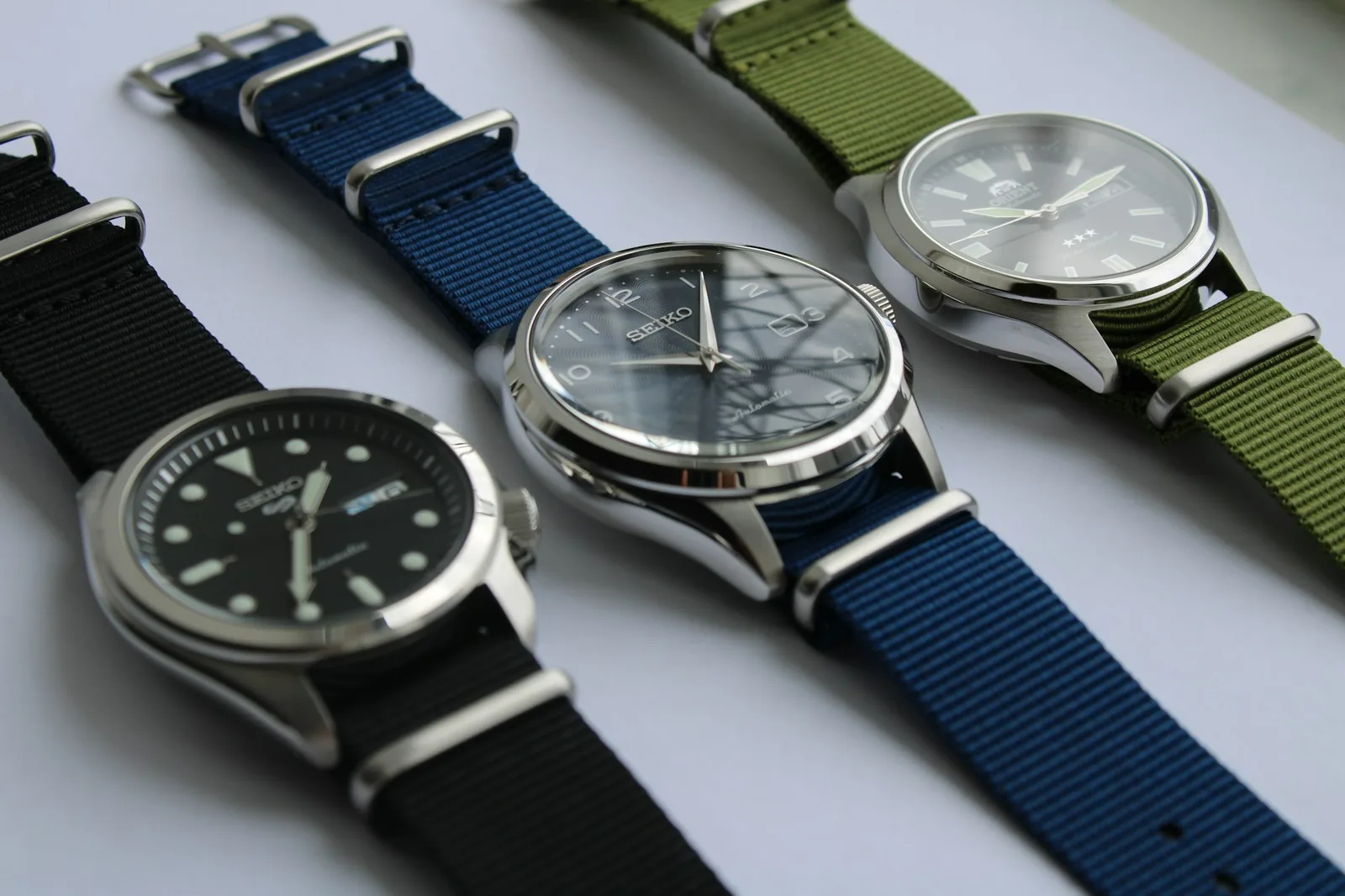 Two wristwatches with different dials lying side by side on a dark slate surface