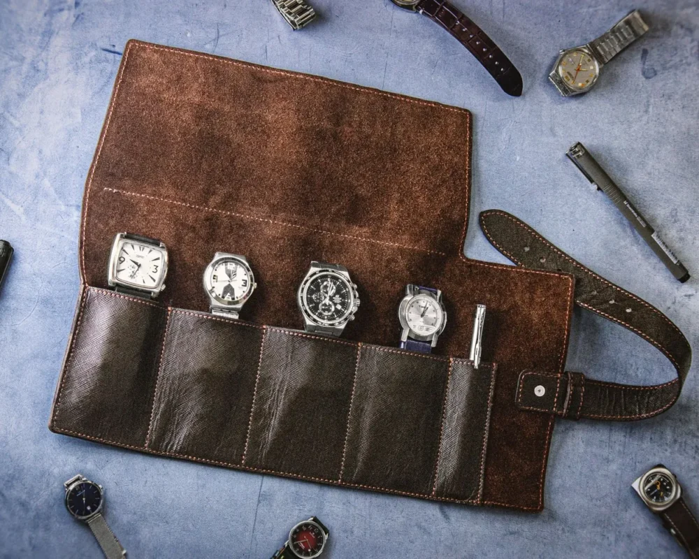 A rolled leather watch case open on a table with a wristwatch inside