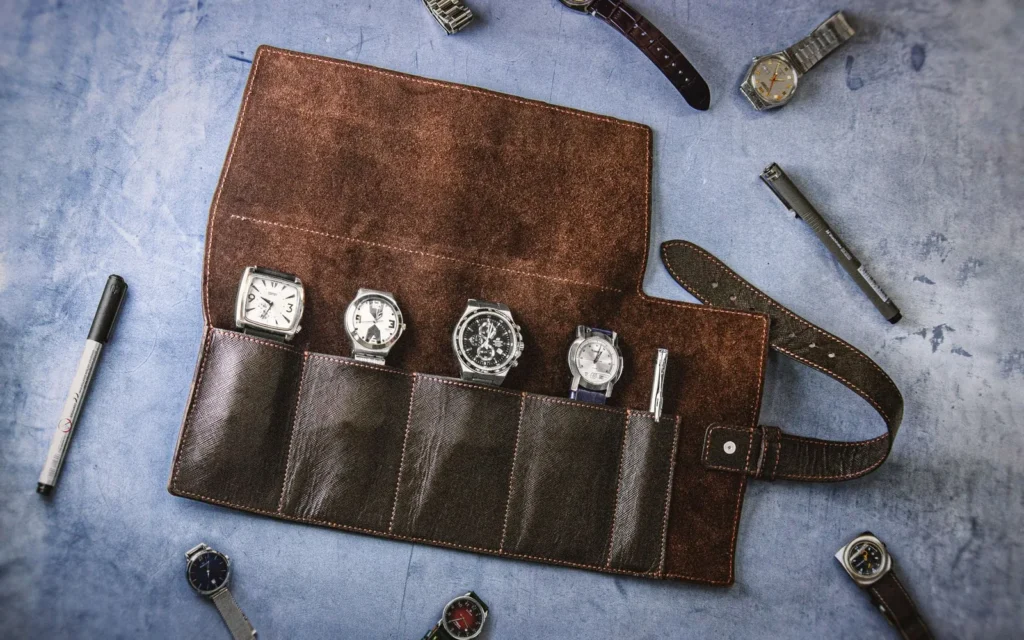 A rolled leather watch case open on a table with a wristwatch inside