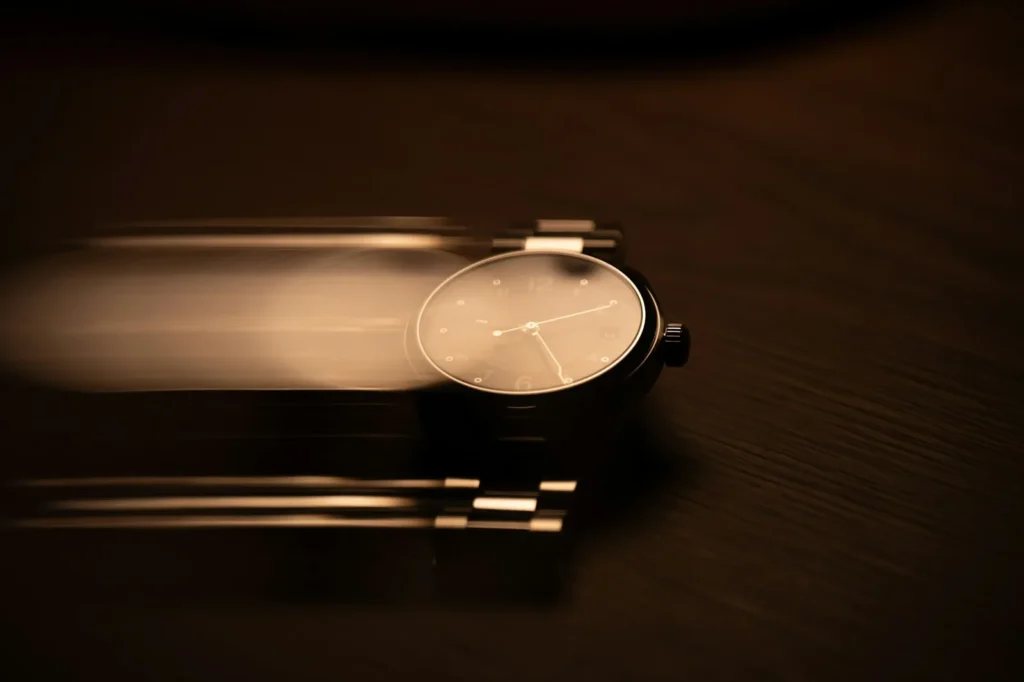A wristwatch with its hands stopped, lying on a dark surface under directional light