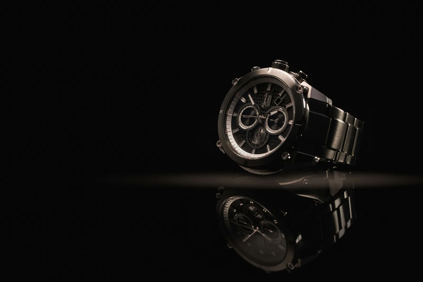 A wristwatch with its hands stopped, lying on a dark surface under directional light