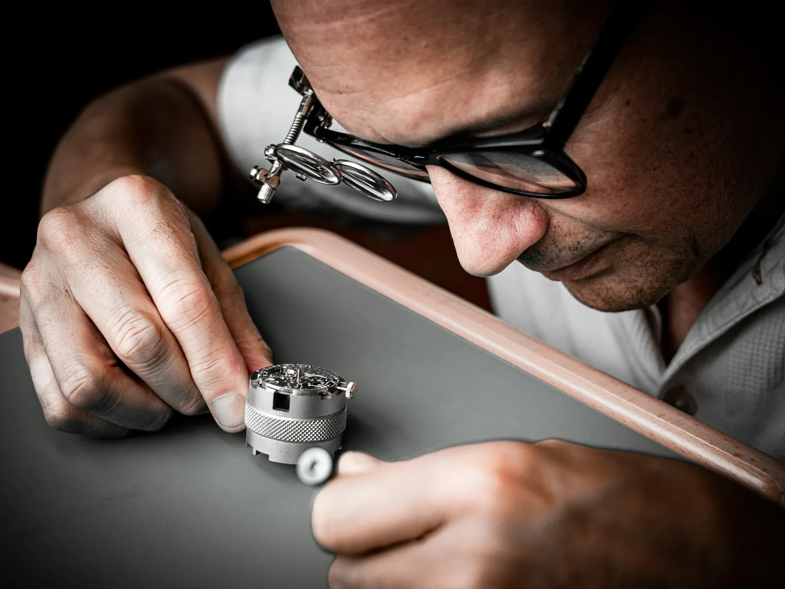 A watchmaker wearing an eye loupe inspecting the inside of a watch movement