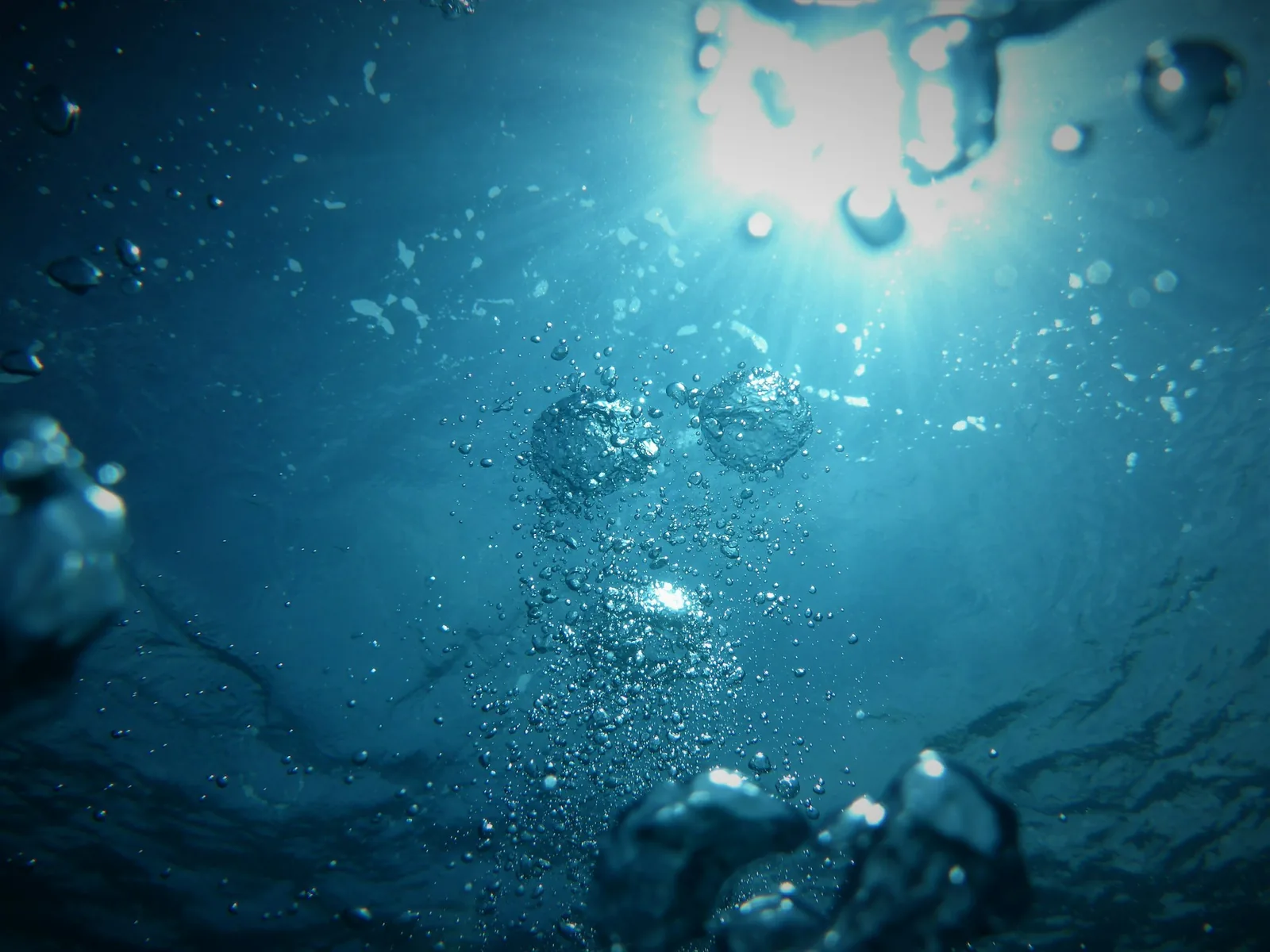 A swimmer moving underwater in a pool with a trail of bubbles