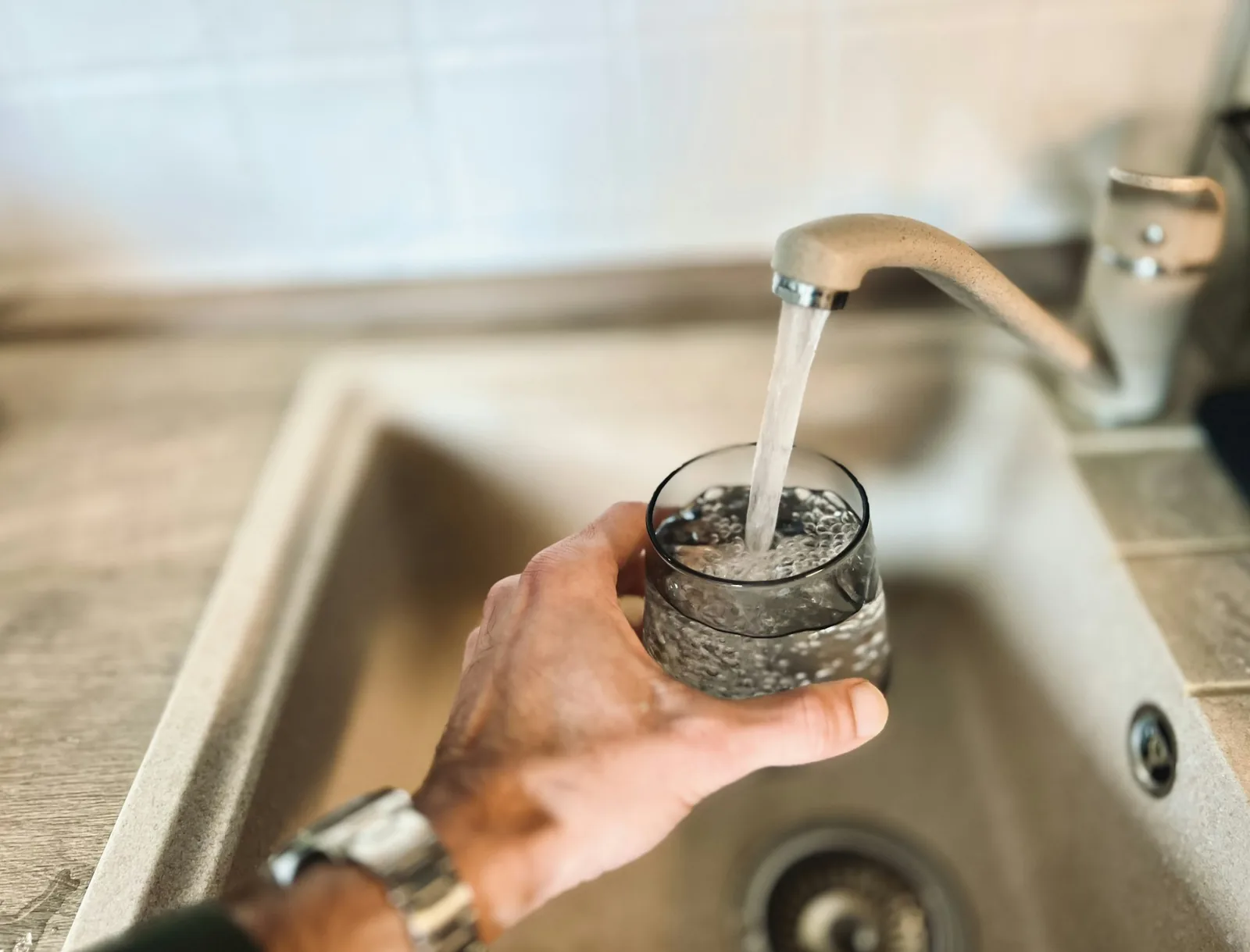 A wristwatch being rinsed under a running tap over a sink