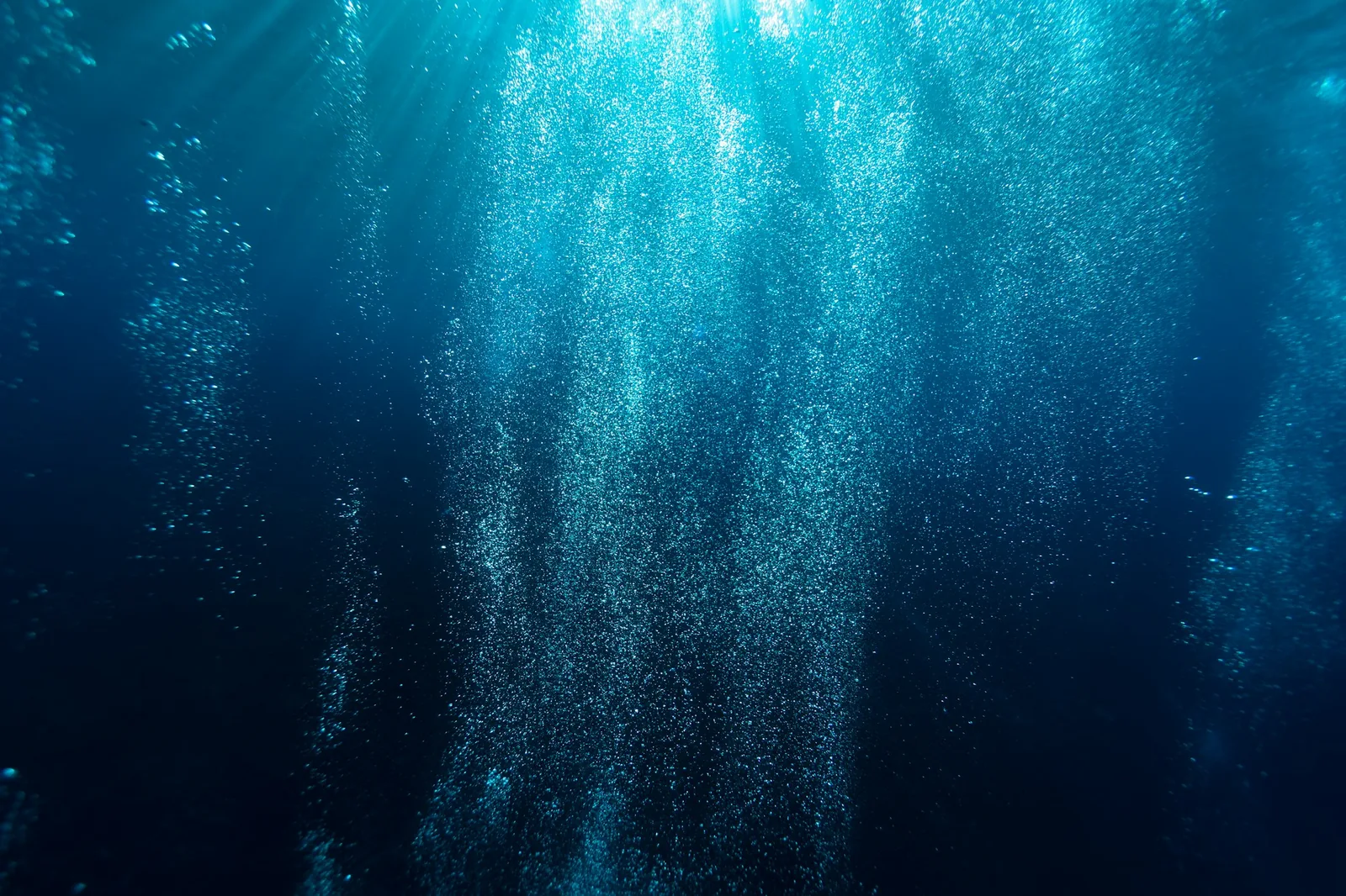 A dive watch photographed underwater with bubbles rising past the bezel